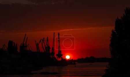 Téléchargez les photos : Grues au port sur un coucher de soleil rouge - en image libre de droit
