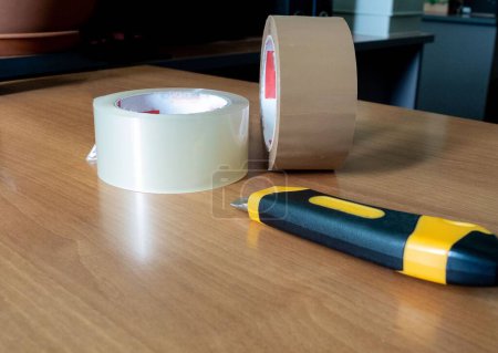 Photo for Packing tape and a box cutter are lying on the table - Royalty Free Image