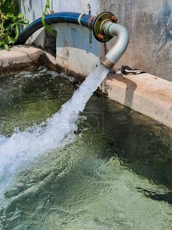 Téléchargez les photos : L'eau d'un puits rempli un étang pour l'irrigation, l'eau d'irrigation de la source, l'écoulement de l'eau d'un grand tube de pompe à la ferme, les agriculteurs pompent l'eau dans les champs. - en image libre de droit