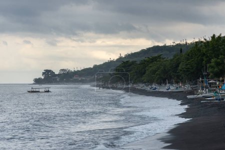 Schwarzer Sandstrand und bedeckter Himmel an der Küste des touristischen Amed-Dorfes auf der Insel Bali, Bezirk Karangasm