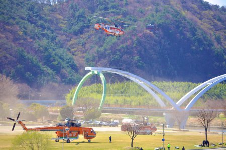 Photo for A dynamic scene at Taehwa Park with one firefighting helicopter soaring in the air and two more stationed on the ground, showcasing coordinated emergency response efforts. - Royalty Free Image
