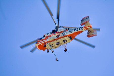 Téléchargez les photos : Vue rapprochée d'un hélicoptère de lutte contre les incendies, mettant l'accent sur les tuyaux suspendus placés dans le vaste ciel bleu, soulignant son état de préparation à l'action. - en image libre de droit