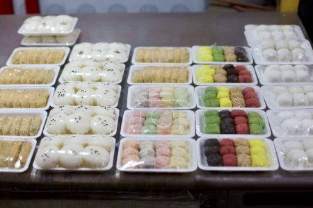 Foto de Tteok cuidadosamente envuelto en saran, un pastel de arroz coreano por excelencia hecho de granos cocidos al vapor y a veces machacados, que se muestra en el vibrante entorno de un mercado coreano tradicional. - Imagen libre de derechos