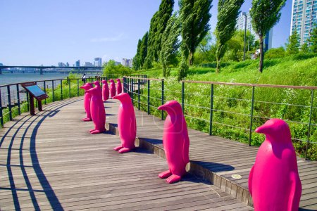 Photo for In a wide-angle shot, meter-tall pink penguins from Hangang Art Park's 'Cracking Art' installation stand out against the wind-swept trees along the Han River. - Royalty Free Image