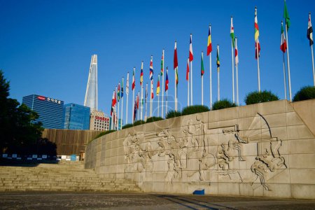 Photo for Seoul, South Korea - June 2, 2023: Intricate figures carved on a wall next to Mongchon Lake in Olympic Park, with flagpoles atop and Lotte World Tower in the distance. - Royalty Free Image