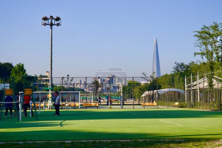Photo for Seoul, South Korea - June 2, 2023: A line of tennis and recreational courts in Gwangnaru Hangang Park, with the towering Lotte Tower visible in the background. - Royalty Free Image