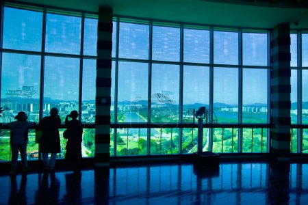 Photo for Hanam City, South Korea - October 1, 2023: Visitors inside the top deck of Hanam Union Tower, observing Misa Boat Race Park through tall wraparound windows, with binoculars. - Royalty Free Image