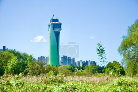 Photo for Hanam City, South Korea - October 1, 2023: Hanam Union Tower stands tall amidst the cityscape, visible from a vantage point amid lush trees and tall grass under a clear blue sky. - Royalty Free Image