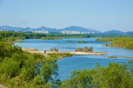 Photo for Hanam City, South Korea - October 1, 2023: A tranquil scene of the Han River, featuring a sandbank and a distant figure, framed by mountains and white apartments. - Royalty Free Image