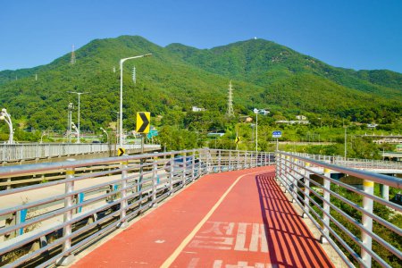 Photo for Hanam City, South Korea - October 1, 2023: A serene bicycle offramp extends from Paldang Bridge, framing the verdant Yebongsan Mountain backdrop. - Royalty Free Image