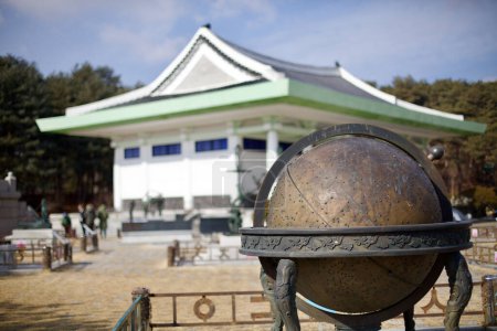 Téléchargez les photos : Yeoju City, Corée du Sud - 16 février 2020 : Une sculpture saisissante sur le globe se dresse bien en vue devant la toile de fond légèrement floue du musée de la tombe du roi Sejong. - en image libre de droit