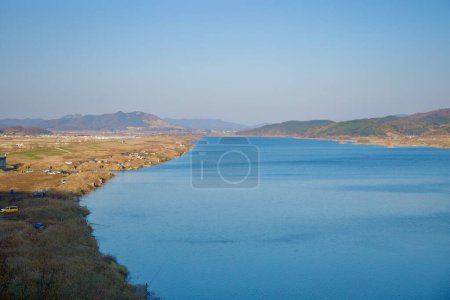 Photo for Sangju City, South Korea - November 18th, 2023: An expansive view of the wide Nakdong River, with adjacent farm fields and low hills in the distance, creating a serene tapestry of natural and agricultural landscapes under the vast Korean sky. - Royalty Free Image
