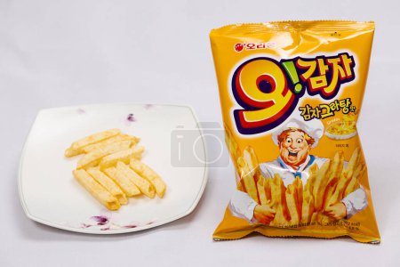 Photo for Ulsan, South Korea - January 14, 2024: A display of O!Karto potato chips, with some chips artfully arranged on a plate beside an unopened bag, highlighting their unique hollow French fry shape and crispy texture, set against a white background. - Royalty Free Image