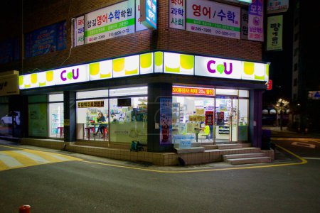 Photo for Ulsan, South Korea - February 20, 2020: A woman enjoys a meal by the window inside a brightly lit CU convenience store, set against the backdrop of a bustling Ulsan city block at night. - Royalty Free Image
