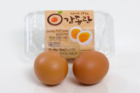 Photo for Ulsan, South Korea - March 6, 2020: Hard-boiled eggs, freshly unpacked from their plastic case, presented in the foreground with the packaging subtly placed in the background, against a clean white backdrop. - Royalty Free Image
