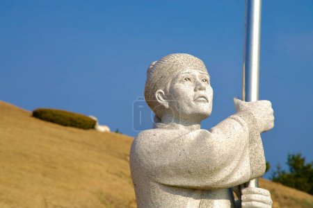 Foto de Samcheok City, Corea del Sur - 28 de diciembre de 2023: Un primer plano de una antigua estatua de piedra guerrera de Silla sosteniendo un poste de metal, mirando hacia arriba contra un cielo azul claro en Lady Suro Memorial Park. - Imagen libre de derechos