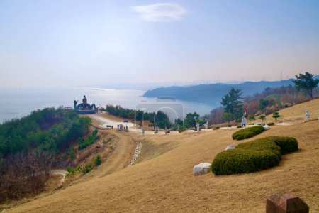 Téléchargez les photos : Samcheok City, Corée du Sud - 28 décembre 2023 : Pelouses roulantes menant à une sculpture dans le parc commémoratif Lady Suro, avec des statues le long du chemin et la mer de l'Est et les montagnes côtières en arrière-plan. - en image libre de droit