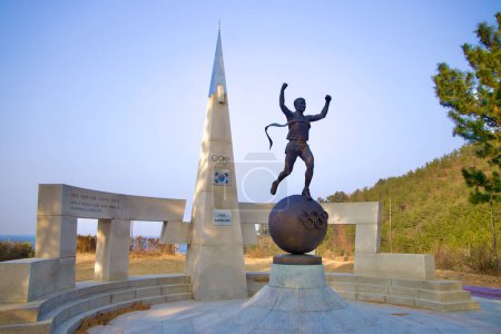 Photo for Samcheok City, South Korea - December 28, 2023: Side view of Hwang Young-jo's statue with a tall pyramid and the Korean flag in the background, symbolizing his Olympic marathon triumph. - Royalty Free Image