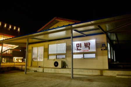 Téléchargez les photos : Comté de Yeongdeok, Corée du Sud - 28 décembre 2023 : Un minbak simple d'un étage près du port de Ganggu offre un aperçu de l'hébergement traditionnel coréen, accueillant les voyageurs avec son éclat chaleureux contre la nuit. - en image libre de droit