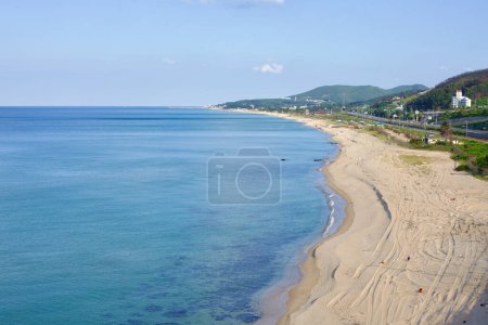 Téléchargez les photos : Gangneung City, Corée du Sud - 29 juillet 2019 : Une vue surélevée capture les longs rivages sablonneux de Mangsang Beach et les vagues ondulantes de la mer de l'Est le long d'un littoral croissant, encadré par des collines basses au bord de la mer sous un ciel bleu. - en image libre de droit