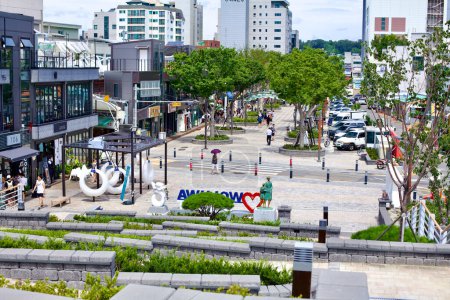 Foto de Gangneung City, Corea del Sur - 29 de julio de 2019: Desde la parte superior de la escalera al final de Wolhwa Street, una vista hacia Wolhwa Street y Gangneung Jungang Market, mostrando la vibrante vida urbana y los espacios verdes de la zona. - Imagen libre de derechos