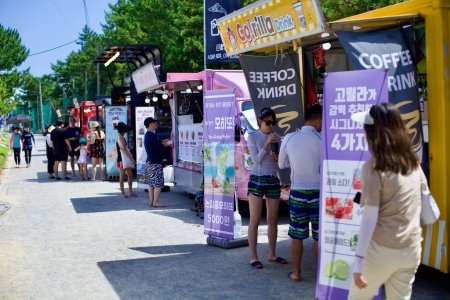 Téléchargez les photos : Gangneung City, Corée du Sud - 29 juillet 2019 : Les clients profitent du café et de la nourriture d'une gamme de camions de nourriture le long de la passerelle à la plage Jigyeongri, mélangeant les loisirs de plage avec la commodité de la nourriture de rue. - en image libre de droit