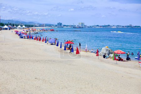 Photo for Gangneung City, South Korea - July 29th, 2019: A vibrant scene at Yeongjin Beach, featuring boats in the East Sea, colorful parasols in the sand, and beachgoers enjoying the day, with Jumunjin Port visible in the distance. - Royalty Free Image