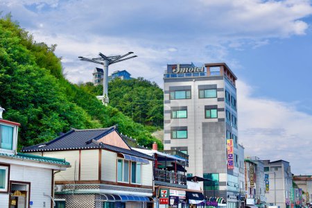 Foto de Donghae City, Corea del Sur - 28 de julio de 2019: Situado en la base de la colina debajo del faro de Mukho, una encantadora colección de moteles, restaurantes y cafeterías prospera, en un contexto de exuberantes árboles verdes en las colinas y un azul claro s - Imagen libre de derechos