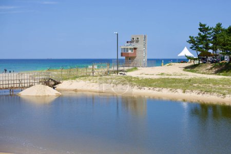 Téléchargez les photos : Comté de Yangyang, Corée du Sud - 30 juillet 2019 : Une tour de guet et une clôture en fil de rasoir marquent la sortie du lac Hyang dans la mer orientale au parc Jigyeong, avec l'horizon s'étendant sur des plages de sable fin. - en image libre de droit