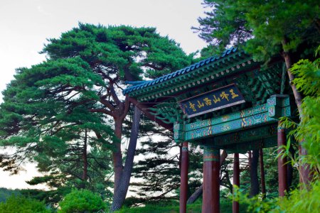 Foto de Condado de Yangyang, Corea del Sur - 30 de julio de 2019: La puerta de entrada verde al histórico Templo de Naksan, rodeada de pinos, marca una entrada serena al final del día a este sitio espiritual de 1500 años de antigüedad.. - Imagen libre de derechos