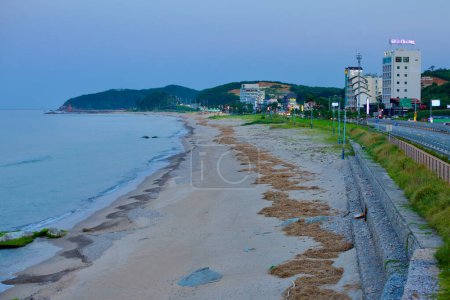 Foto de Condado de Yangyang, Corea del Sur - 30 de julio de 2019: Una vista hacia el sur de Jeongam Beach al caer la noche, mostrando hoteles y moteles a lo largo de la carretera que conduce a una colina costera baja. - Imagen libre de derechos