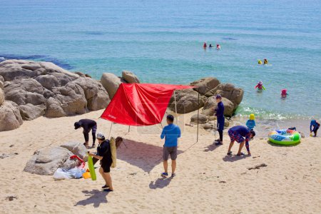 Foto de Condado de Goseong, Corea del Sur - 30 de julio de 2019: En las costas arenosas de Gonghyeonjin Beach, una familia instala una tienda emergente cerca de impresionantes formaciones rocosas, con niños jugando en el agua y adultos preparándose para un día de relajación junto a la playa.. - Imagen libre de derechos