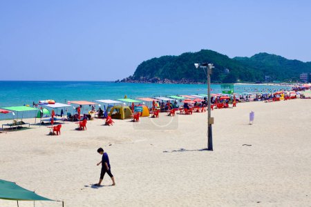 Téléchargez les photos : Comté de Goseong, Corée du Sud - 31 juillet 2019 : De l'extrémité nord, le sable immaculé de la plage de Hwajinpo se déploie vers les montagnes balnéaires, sous le ciel clair d'une journée d'été brillante, avec des tentes parsemant le rivage. - en image libre de droit