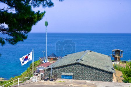 Téléchargez les photos : Comté de Goseong, Corée du Sud - 31 juillet 2019 : Niché sous le phare de Daejin, un bâtiment policier et militaire sert de belvédère stratégique sur les eaux calmes et bleues de la mer de l'Est, avec le drapeau coréen fièrement affiché au premier plan. - en image libre de droit