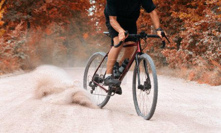 Ciclista en paseos en bicicleta a lo largo de la carretera de grava levantando el polvo de la rueda trasera en el bosque de otoño. Ciclismo de grava. Concepto de deportes extremos y actividad.