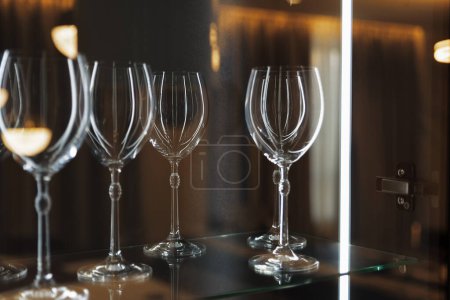 Photo for Wine glasses on a glass shelf with lighting. Empty crystal glasses close-up. - Royalty Free Image