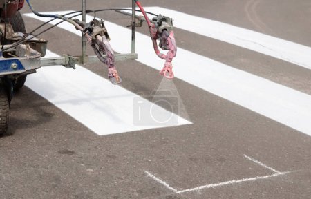 Foto de Los trabajadores de la ciudad pintan carriles de cruce en la carretera. Pintura máquina pinta rayas en asfalto para peatones. - Imagen libre de derechos