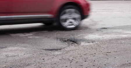 Photo for The car goes around a pothole on the road. Broken asphalt after winter. Road repair. - Royalty Free Image