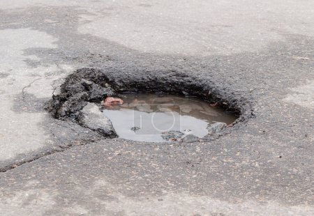 Damaged road after winter. Deep pit on the asphalt with puddle. Road repair. Traffic danger.