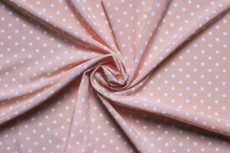 Texture of twisted pink fabric with white dots. Fabric is twisted into a bundle in the center.