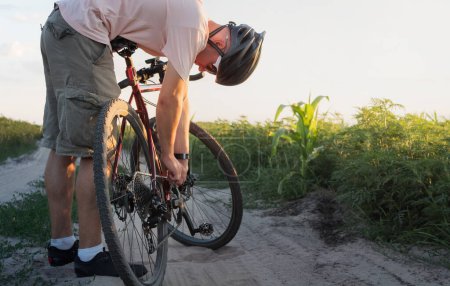 A cyclist repairs a bicycle chain in a field. Breakdown in inappropriate conditions.