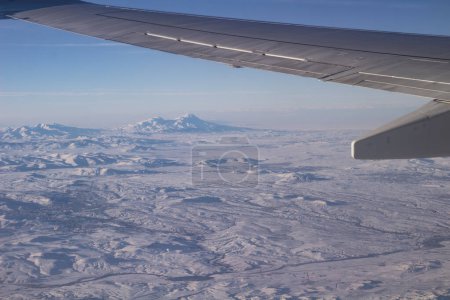 Der Himmel mit Wolken und schneebedeckten Bergen. Foto aus dem Flugzeug. Flügel eines Flugzeugs am Himmel.