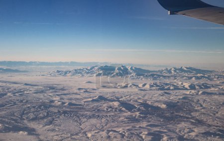 Photo for The sky with clouds and mountains in snow. Photo taken from an airplane. Wing of a plane in the sky. - Royalty Free Image