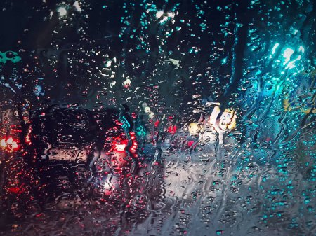 Photo for Winter night urban traffic scene as seen through the vehicle window covered with sleet drops. Melting snow water drips on the car windshield - Royalty Free Image