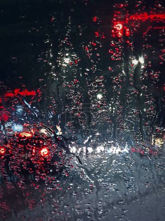 Photo for Winter night urban traffic scene as seen through the vehicle windscreen covered with sleet drops. Melting snow water drops on the car windo - Royalty Free Image