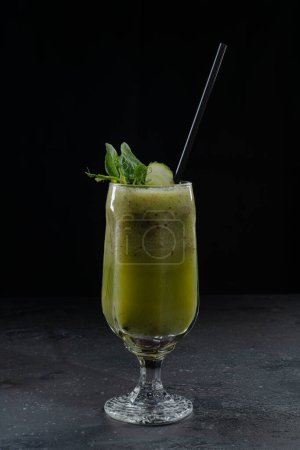 green smoothie in a glass on a black background with cucumber spinach celery apple ice for summer restaurant cocktail menu
