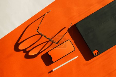 Photo for Electronic device blank screen mockup. Orange color. Smart phone and graphic tablet. Glasses shadow. - Royalty Free Image