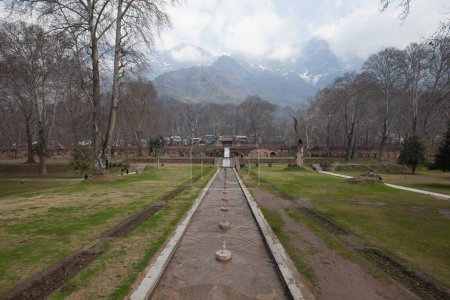 A park in Srinagar, India, with a bridge walkway, a village and a large mountain range in the background.