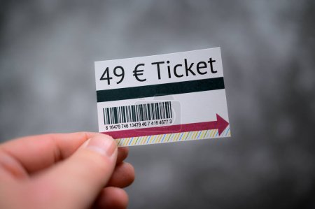 Hand hält 49 Euro Ticket-Attrappe vor grauem Hintergrund mit Barcode und minimalen Designelementen 
