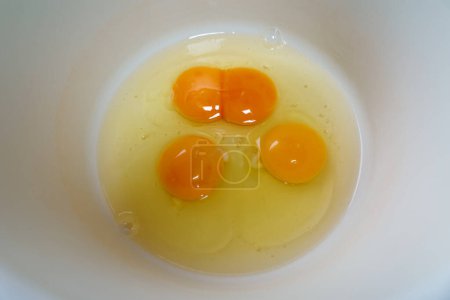 Photo for Three raw eggs with double yolk in one, in a white bowl, top view, close up shot. - Royalty Free Image